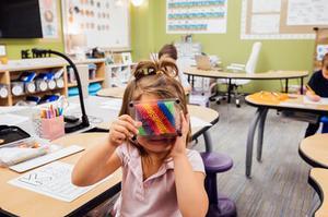 A photo of a young girl in a classroom pressing her face into pin art.